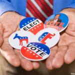 Close-up of hands holding five political election buttons or badges.