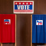 Front view of two voting booths in a polling place, one with a red curtain and the Republican elephant, the other with a blue curtain and the Democratic donkey. ©Hill Street Studios/Blend Images LLC/Glow Images. MHE World.