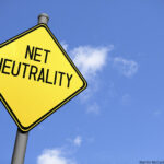 Low-angle view of a yellow warning sign with the text 'Net Neutrality' against a blue sky.