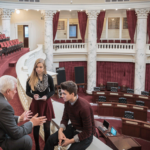 High-angle three-quarter-length view of two teenagers talking to a male politician in the senate gallery of the Idaho State Capitol building, Boise, Idaho