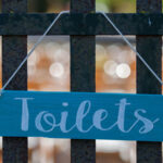 arrow-shaped sign on fence with the word toilets on sign