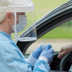 in full protective gear a healthcare worker collects a sample from a man sitting inside his car