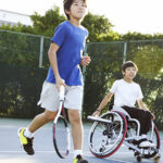 A teenage boy running with another teenage boy in a wheelchair
