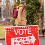 Election voters at a polling place. A Photo ID required sign is visible.