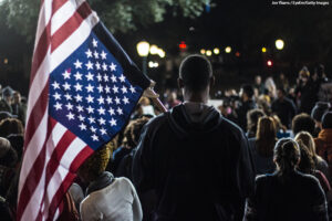 Man in crowd holding an upside down American flag.