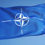 NATO flag waving against clean blue sky, close up