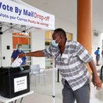 A poll worker casts a mail-in ballot for a disabled driver in East Tampa, Florida on August 16, 2020.